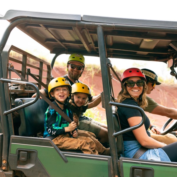 Family in helmets riding an off-road vehicle outdoors.