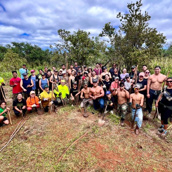 Group of people with gardening tools in a field, surrounded by trees.