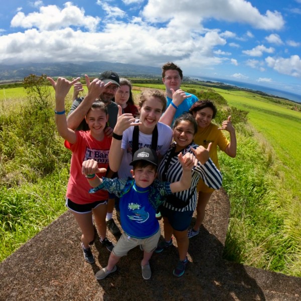 Group of people on a grassy hill, sunny day, with a scenic landscape in the background.