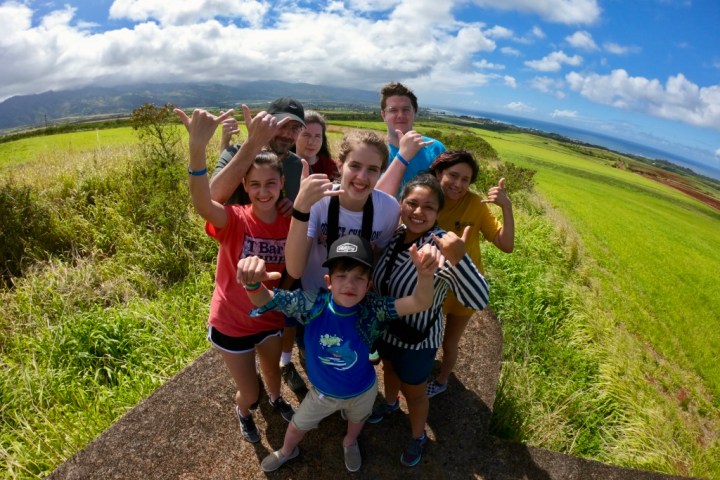 Group of people on a grassy hill, sunny day, with a scenic landscape in the background.