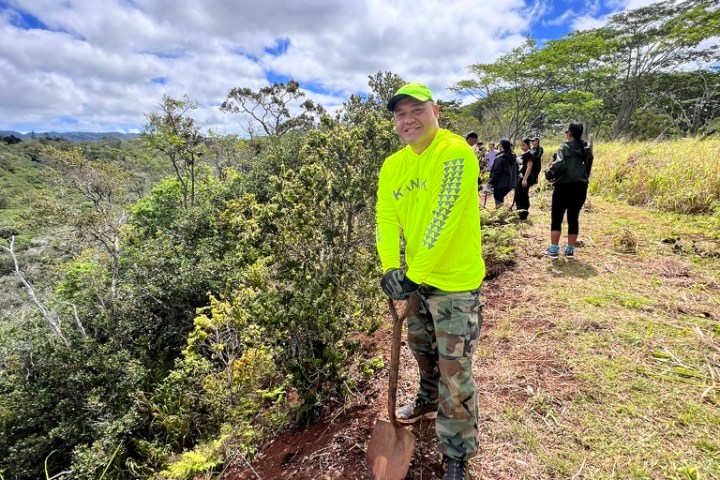 Person in bright attire holding a shovel on a hill with a scenic view.