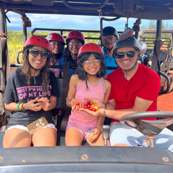 Smiling group in helmets on an off-road vehicle, holding red tomatoes.