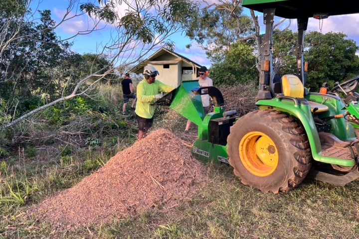 Person operating tractor with wood chipper, creating mulch pile in garden area.