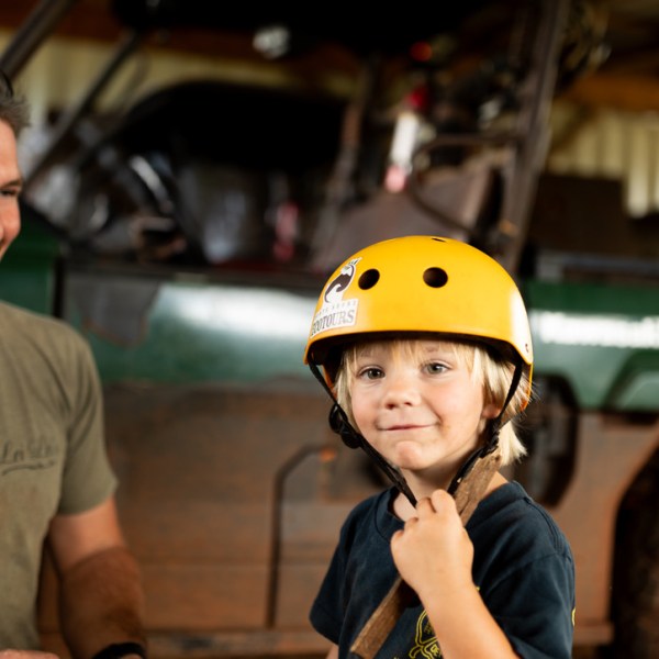 Man smiling beside a child wearing a yellow helmet indoors.