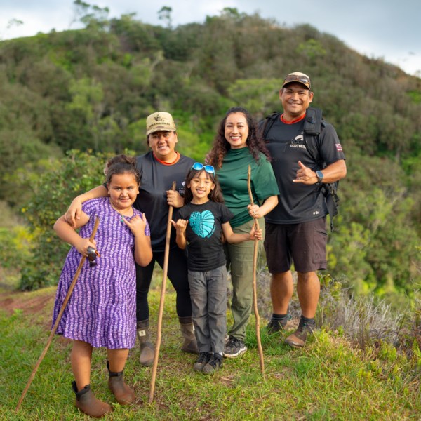 Group of five people with hiking gear, smiling on a grassy hill path.