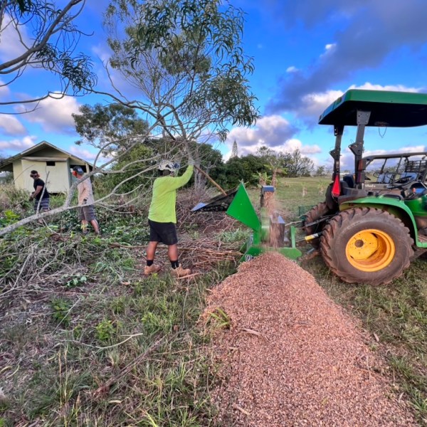 Two people using a wood chipper near a tractor in a rural area.