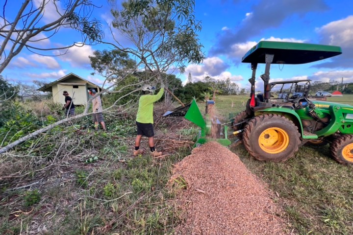 Two people using a wood chipper near a tractor in a rural area.