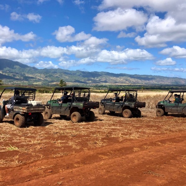 Four off-road vehicles parked on a dirt path with mountains in the background.
