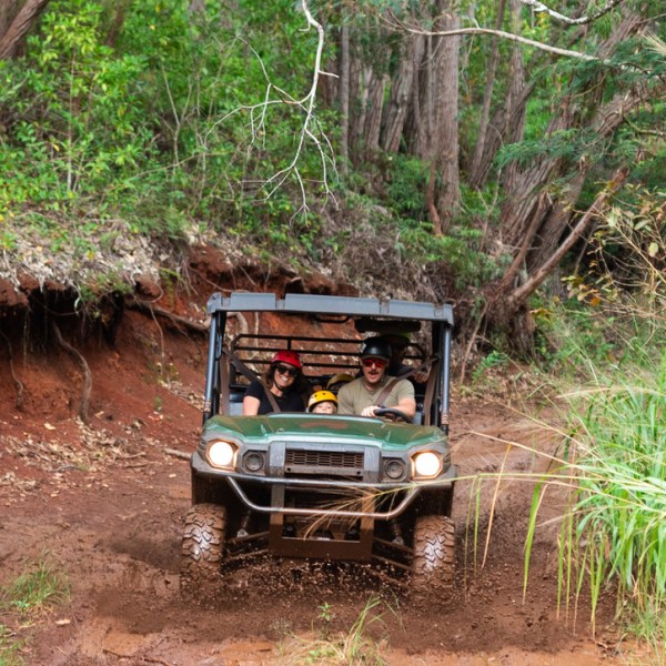 Off-road vehicle with people driving through a muddy forest trail.